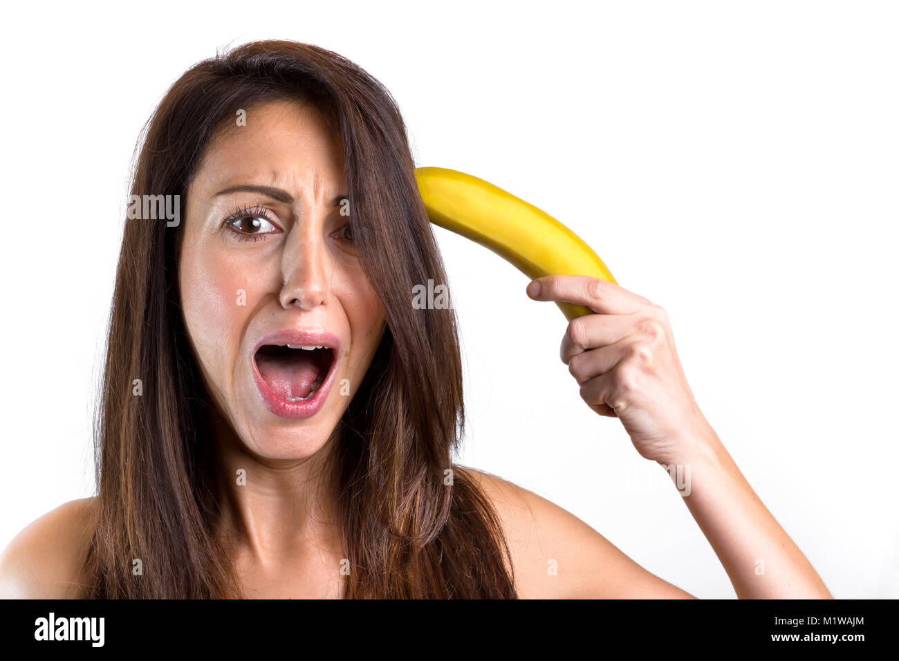 A funny portrait of a beautiful girl trying to shoot herself with a banana gun, while screaming. Cute girl having fun over white background. Space for Stock Photo