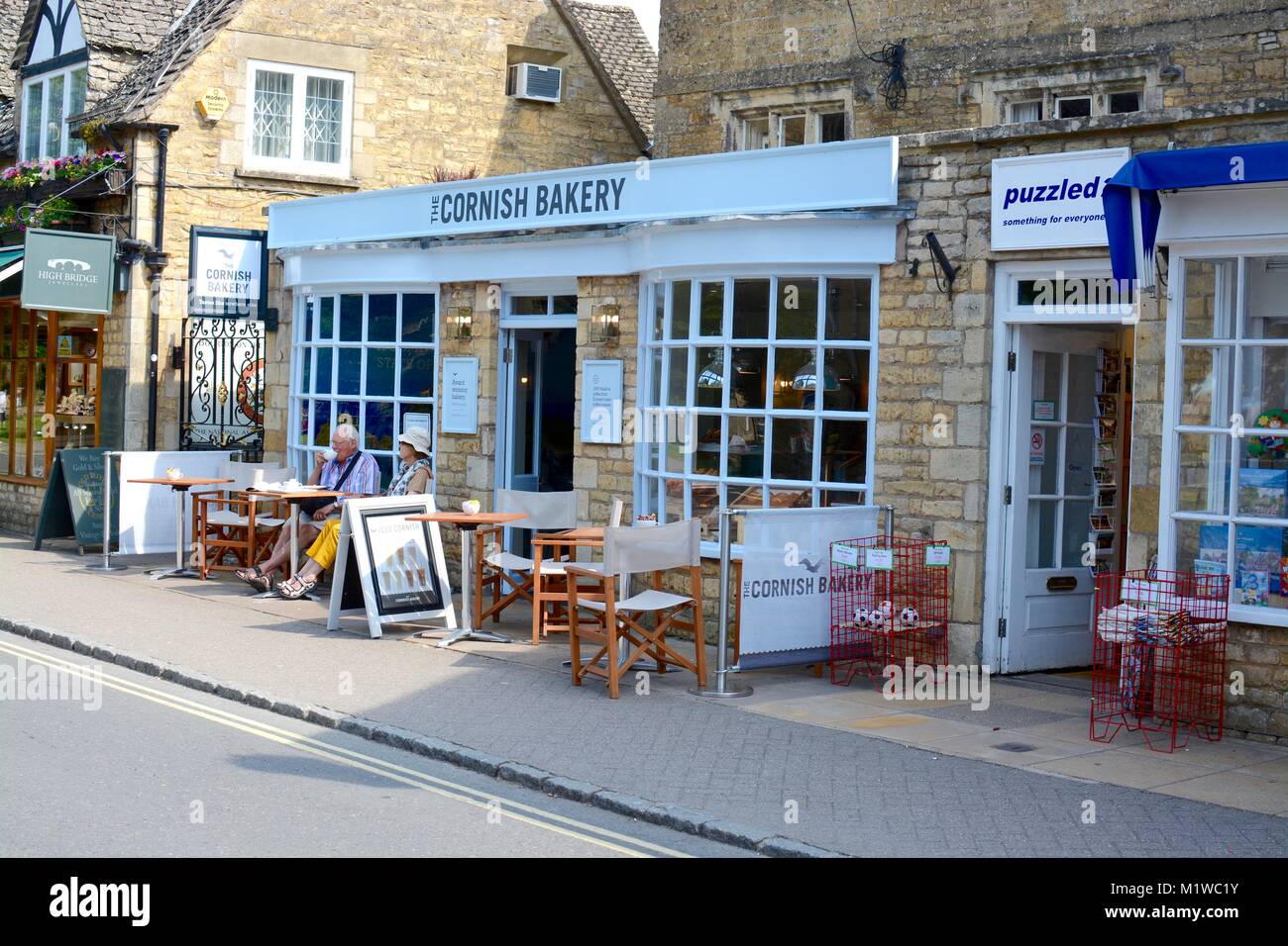People enjoying food and drink at the Cornish bakery, main street, Bourton on the water, Cotswolds, Gloucestershire, UK Stock Photo
