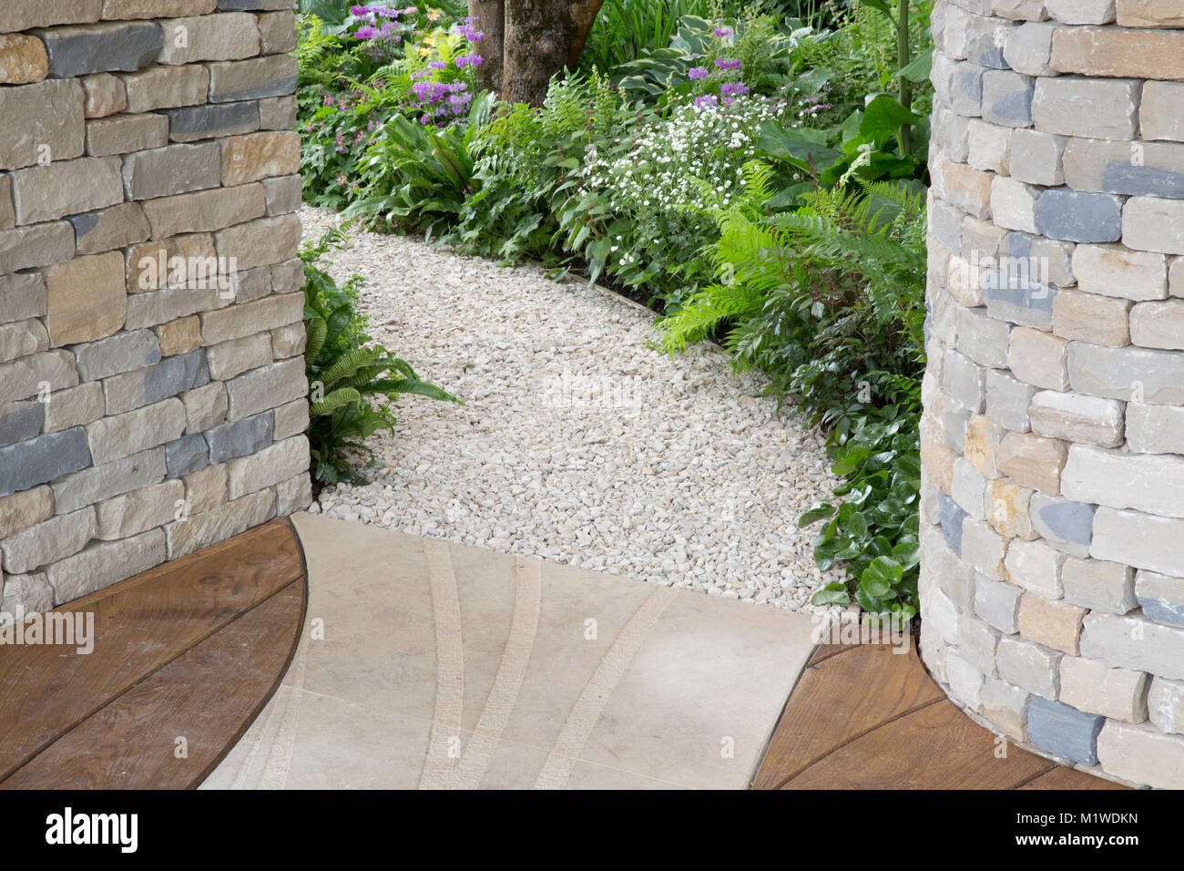 Curved gravel garden path leading through a cottage wild garden with ferns, Chelsea Flower show, Stock Photo