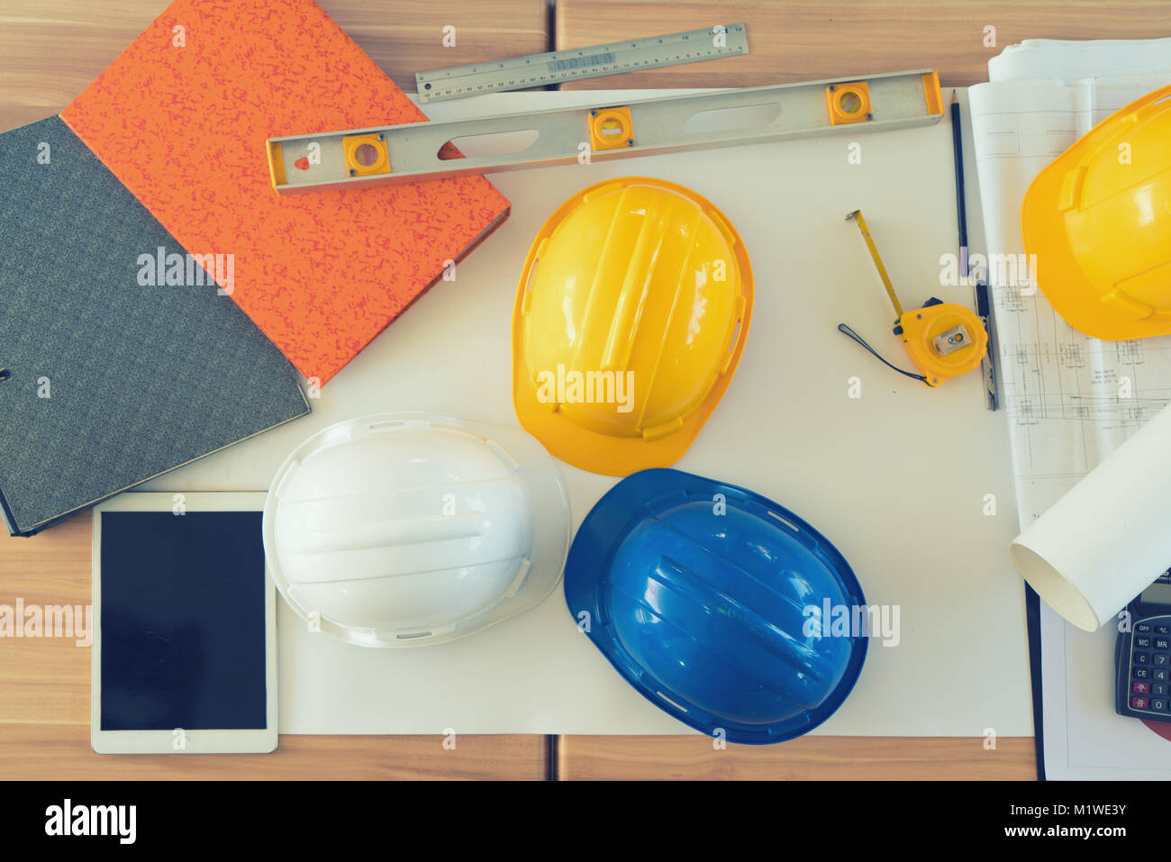 Yellow, white and blue helmet on table with tablet, grey folder,measuring tools and architectural project. Stock Photo