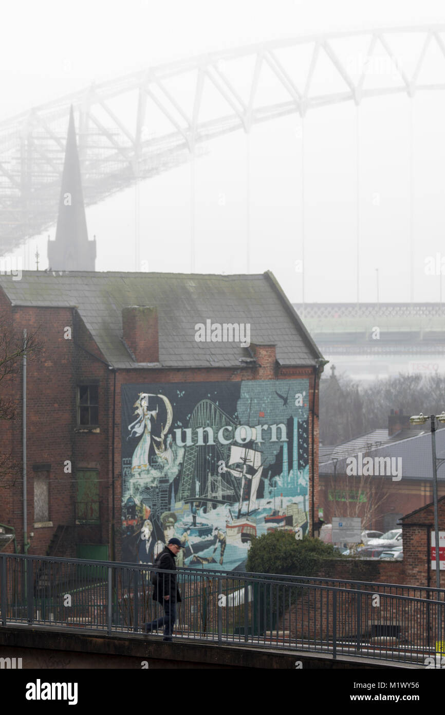 Runcorn, Cheshire, 3rd February 2018. UK Weather. Cold, grey and damp for many today as temperatures get even colder of the weekend with snow for some. A person wrapped up for the weather as he crosses over the Bridgewater Canal in Runcorn with the Runcorn Bridge in the distance on a cold, damp day © DGDImages/Alamy Live News Stock Photo