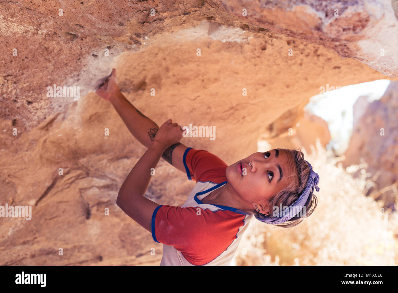 Petite asian woman rock climbing outdoors examines the stone before her climb Stock Photo