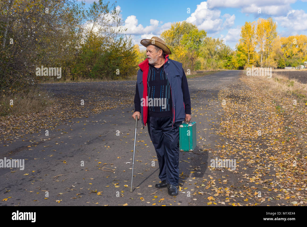 Senior man with walking stick standing on a country road and holing an ...
