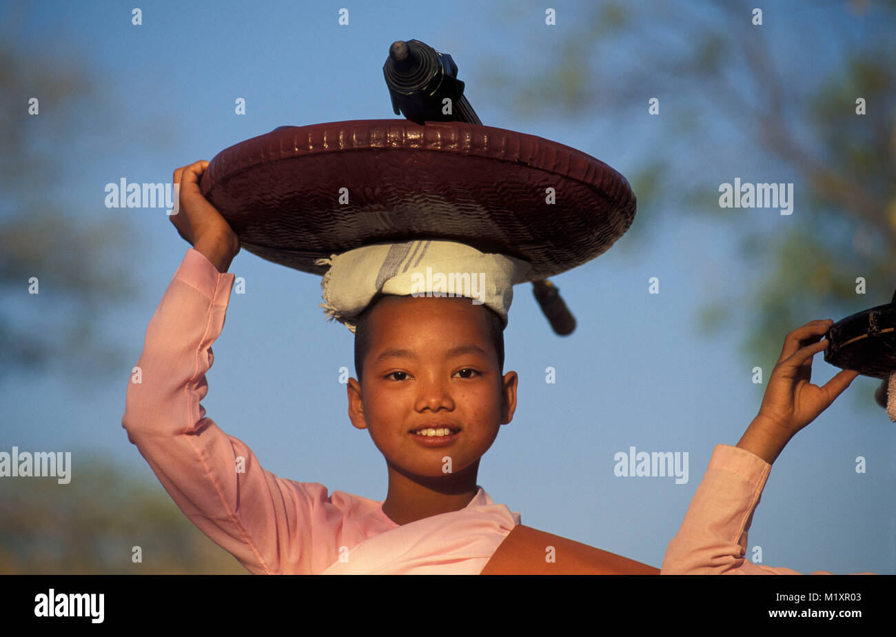 Myanmar (Burma). Bagan (Pagan). Portrait of young Buddhist nun carrying umbrella and plate on head. Gathering food, alms. Stock Photo