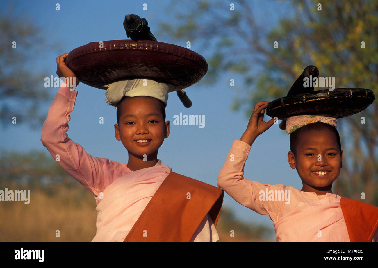 Myanmar (Burma). Bagan (Pagan). Portrait of young Buddhist nuns carrying umbrella and plate on head. Gathering food, alms. Stock Photo