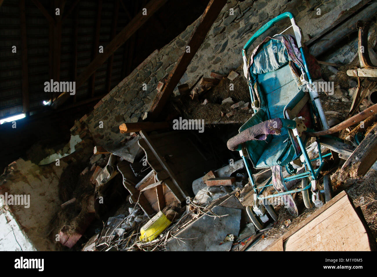 The interior of and old ruin is filled with a mess. An abandoned baby carriage can be seen. Stock Photo