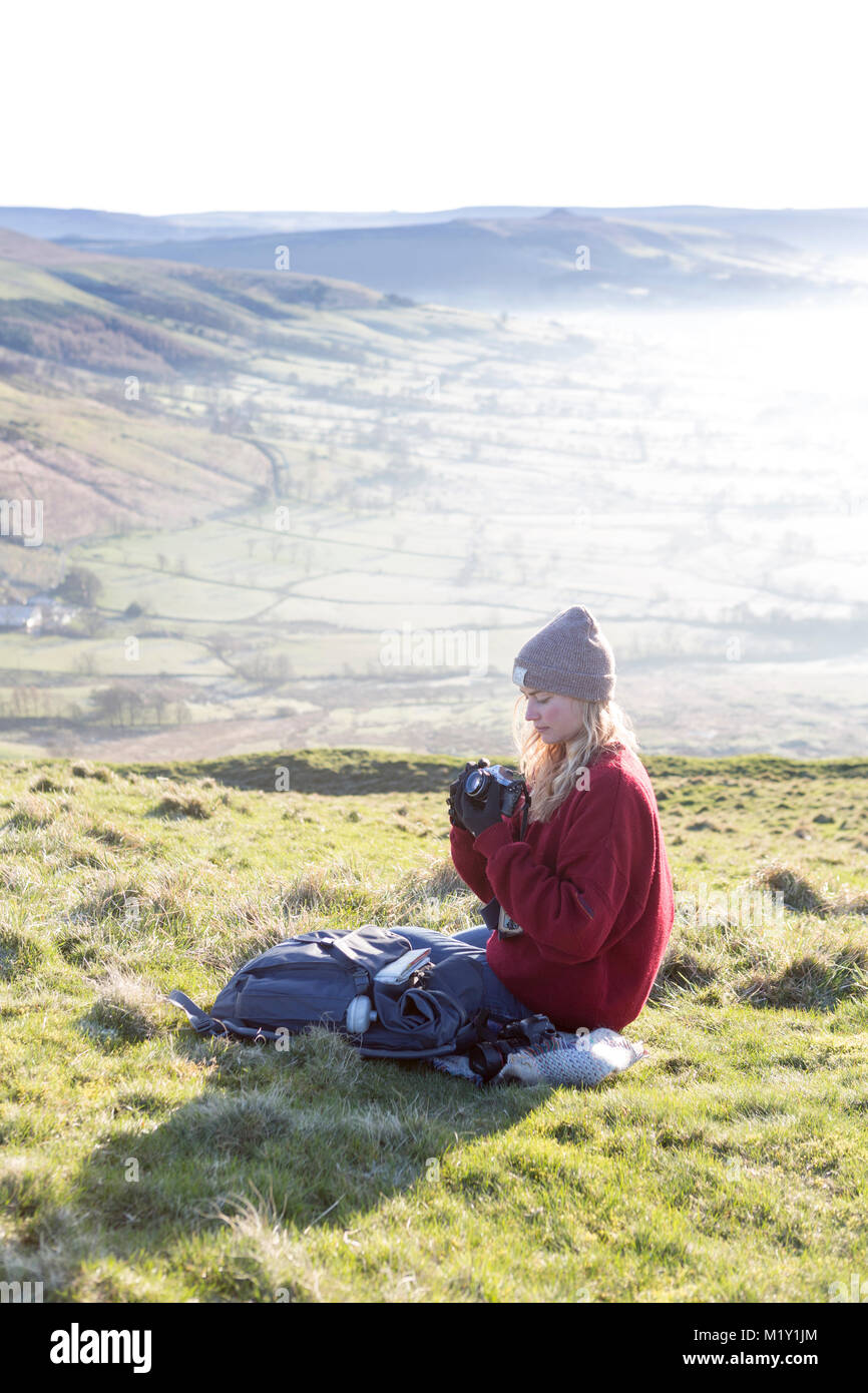 UK, Derbyshire, a walker checking her camera settings  on Mam Tor overlooking Hope Valley. Stock Photo