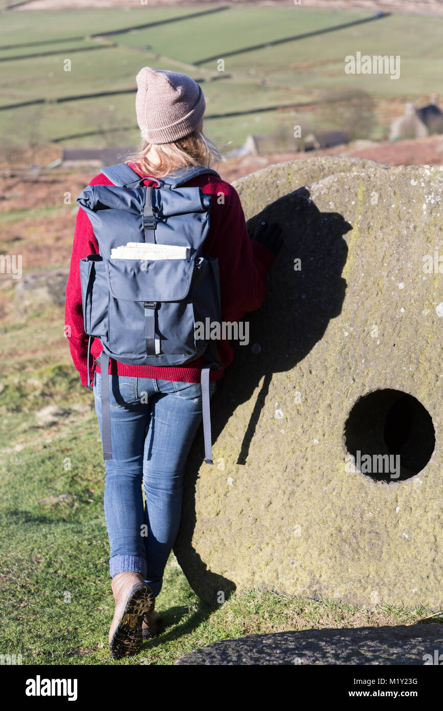 UK, Derbyshire, Peak District Nationa Park, a walker leans against discarded millstones at Stanage Edge. Stock Photo