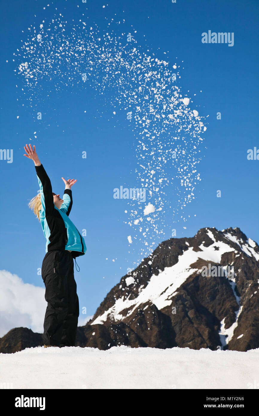 Woman throwing snow in mid-air on top of snowdrift in early spring in the Copper River Delta region of the Chugach National Forest in Alaska. Stock Photo