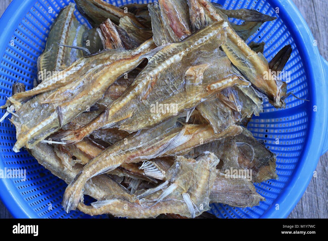 Close up of Dried Fish in blue strainer against wooden background Stock Photo