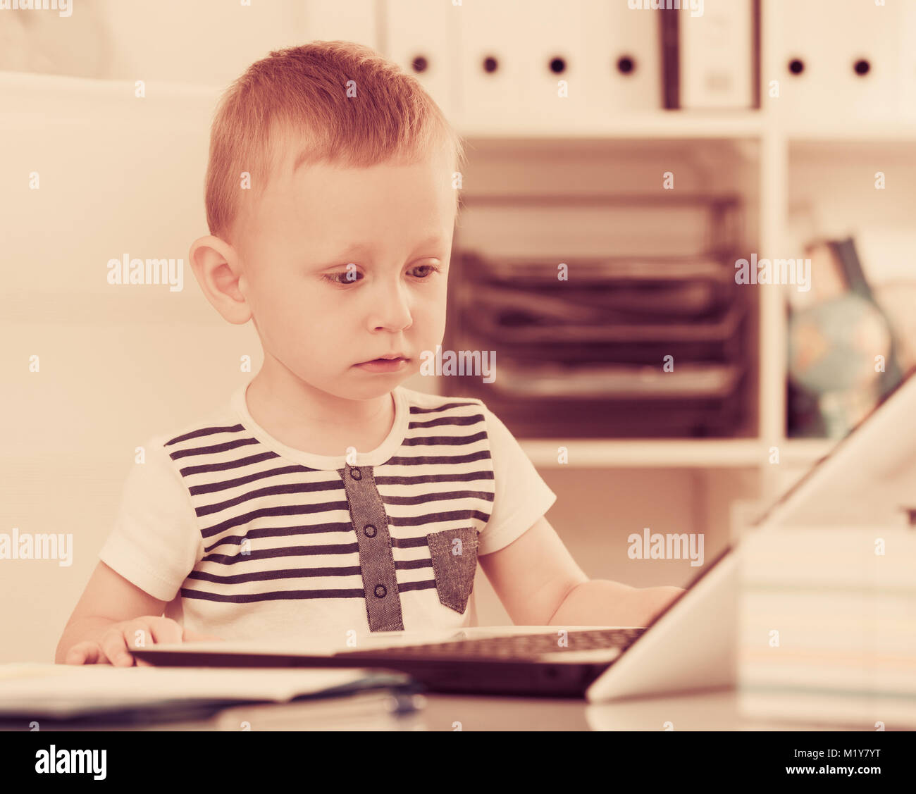 Cute kid is watching cartoons on laptop in the office. Stock Photo