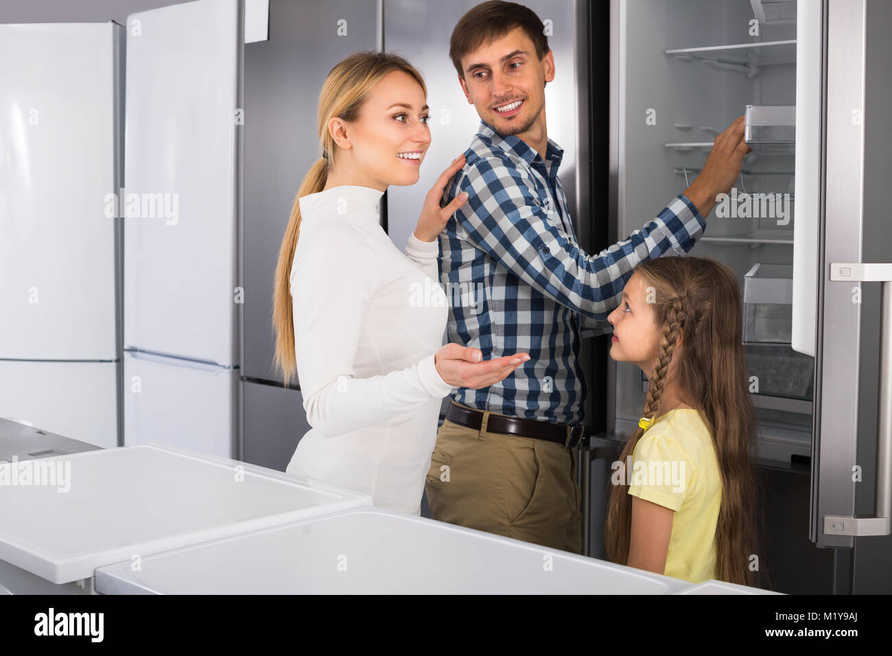 Happy family with girl choosing refrigerator in hypermarket Stock Photo