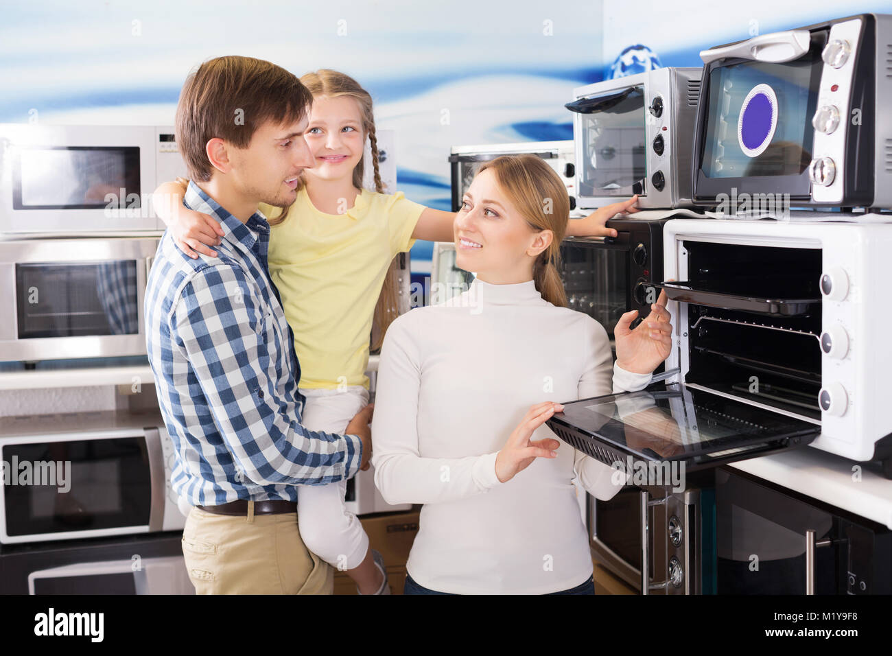 Positivel young man and woman with girl buying modern microwave in store with electronics Stock Photo