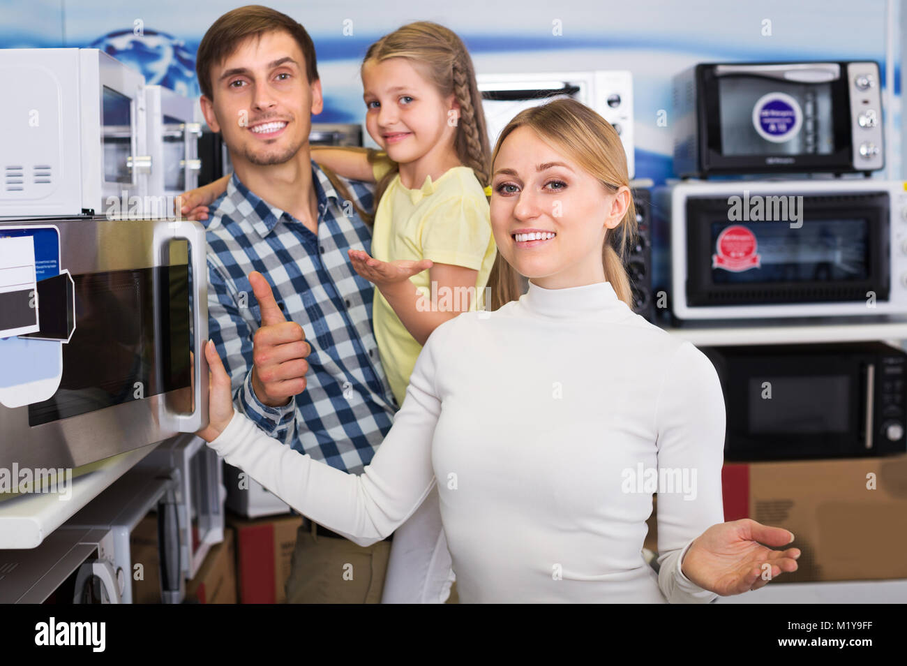 Positivel man and woman with girl buying modern microwave in store with electronics Stock Photo