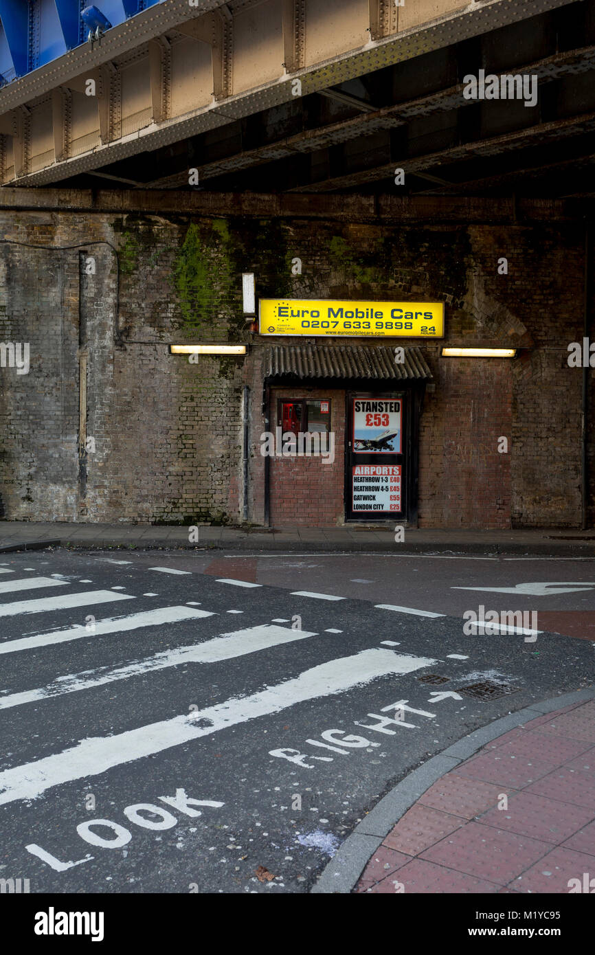 A taxi cab office advertising airport run fairs beneath a Victorian bridge near Waterloo station, on 30th January 2018, in the south London borough of Southwark, England. Stock Photo
