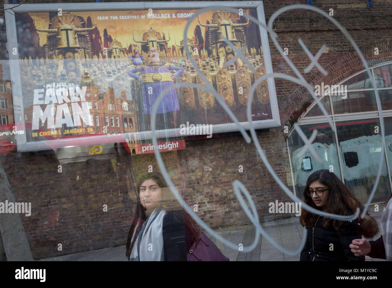 Young women, bus stop graffiti and an ad for the new Aardman Animation's new release Early Man, on 30th January 2018, in the south London borough of Southwark, England. Stock Photo