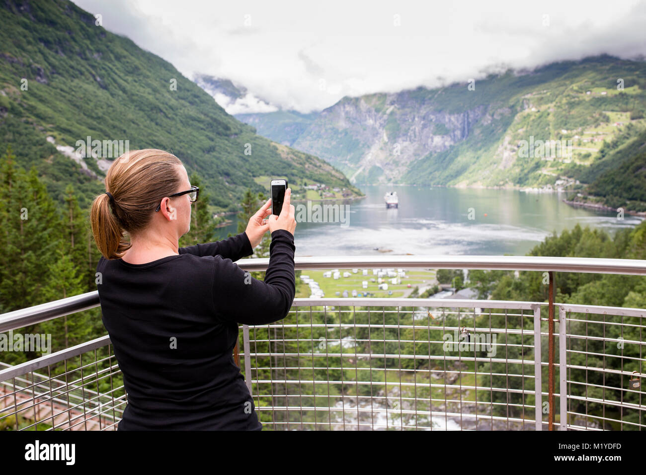 Woman taking a picture with her smartphone in front of a majestic view of a fjord in Norway. Stock Photo