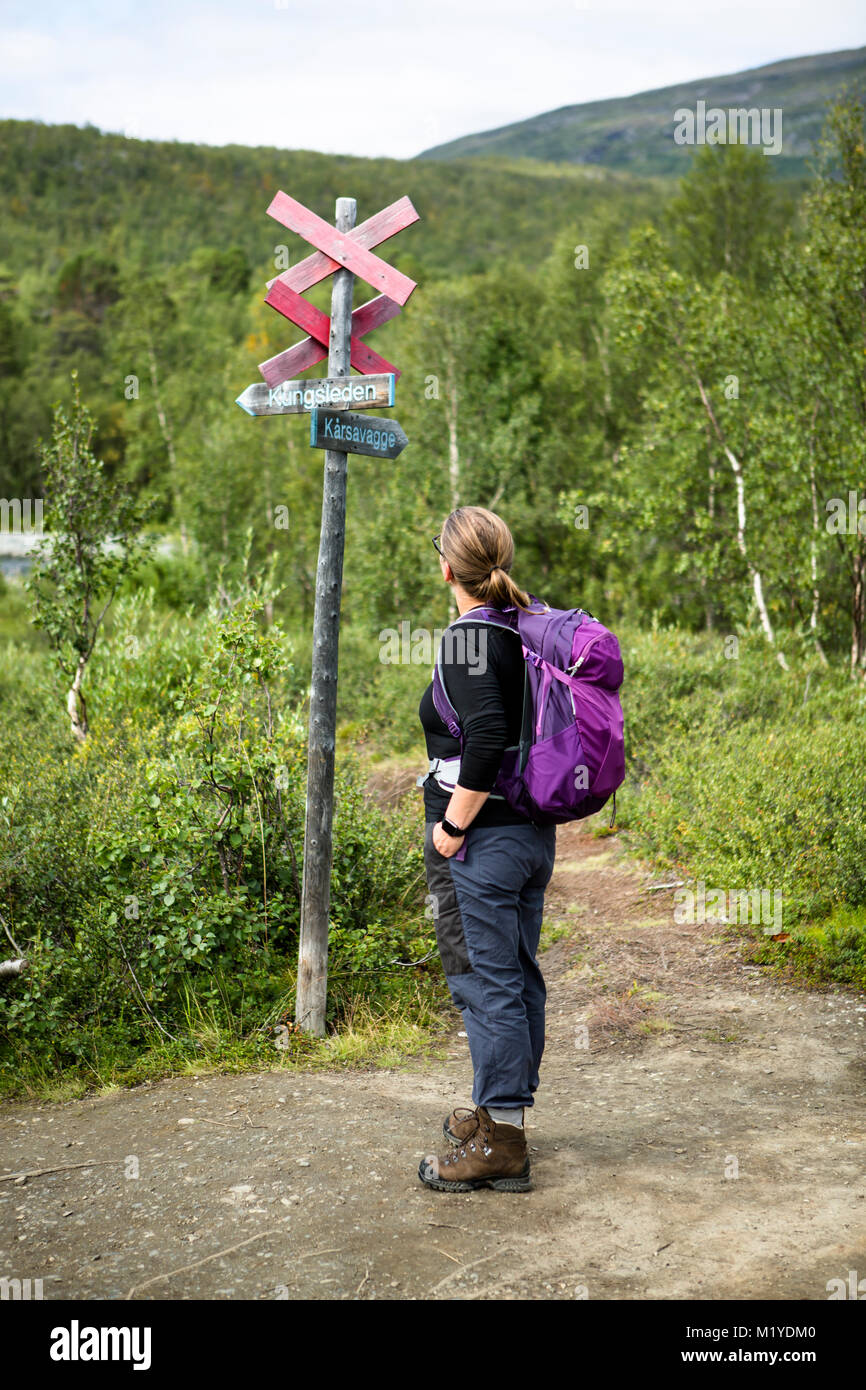 Female with backpack looking at a sign at the walking trail of Kungsleden in Lapland, Sweden. Stock Photo
