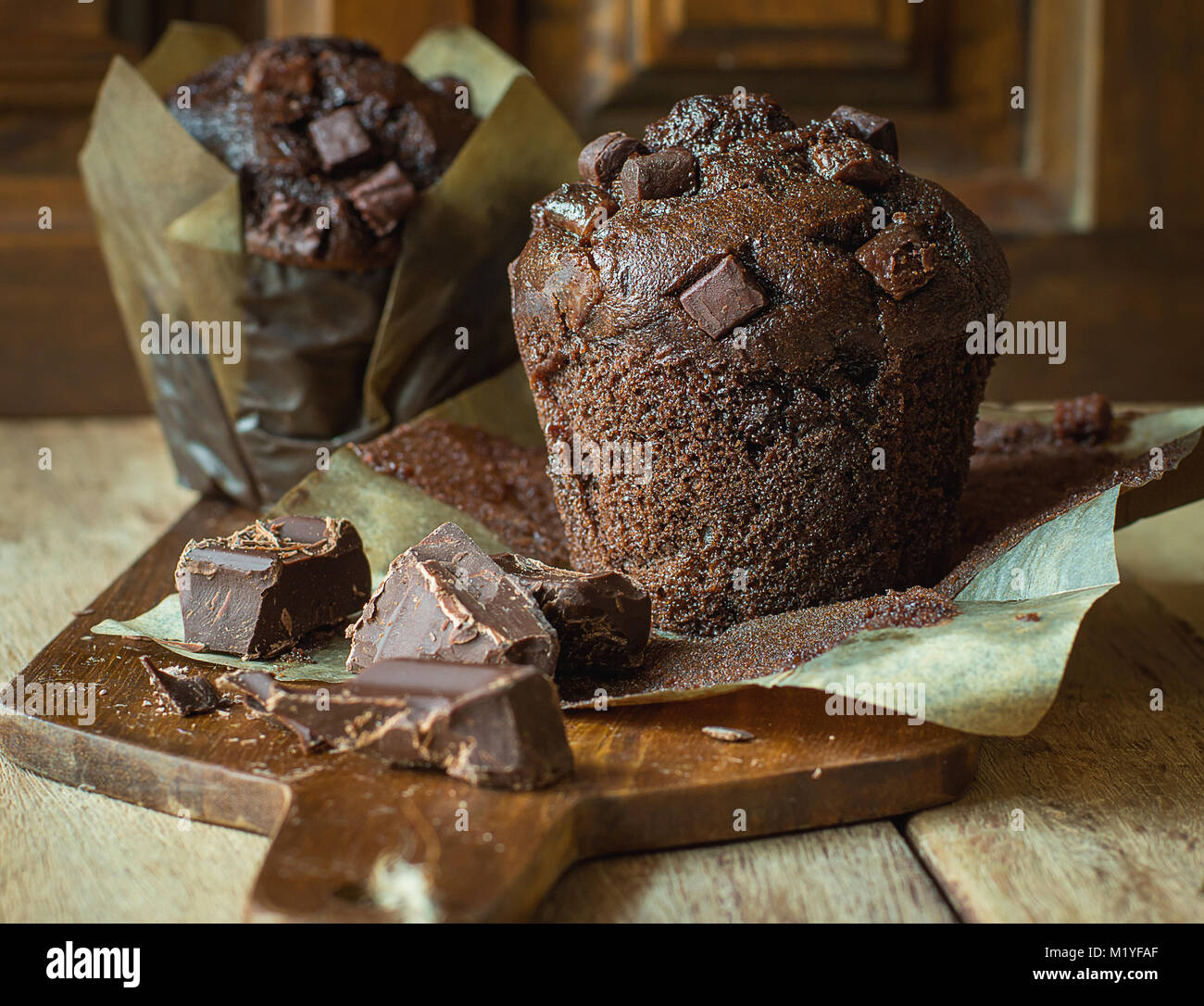 Scrumptious Home Baked Chocolate Chips Muffins in Brown Paper on Wooden Cutting Board. Rustic Kitchen Interior Rural Style. Square Size Stock Photo