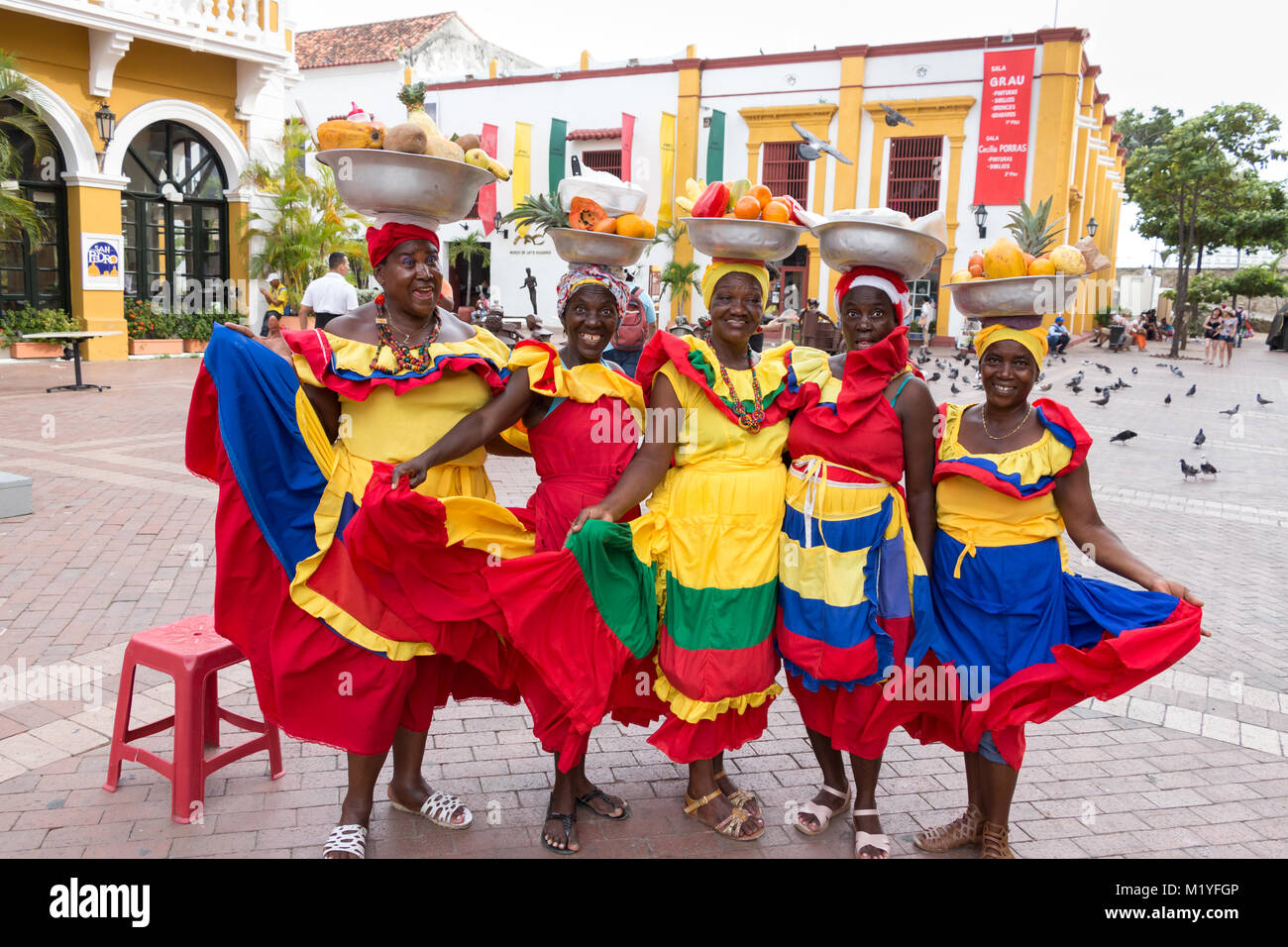 Cartagena, Colombia - January 23th, 2018: Five palenqueras with a metal basket with fruits are posing showing their multicolor traditional dress at th Stock Photo