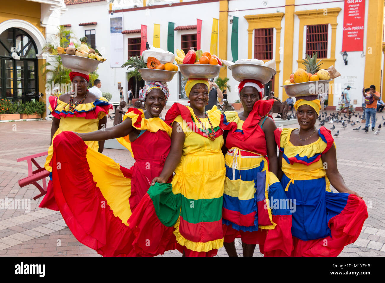Cartagena, Colombia - January 23th, 2018: Five palenqueras with a metal basket with fruits are posing showing their multicolor traditional dress at th Stock Photo
