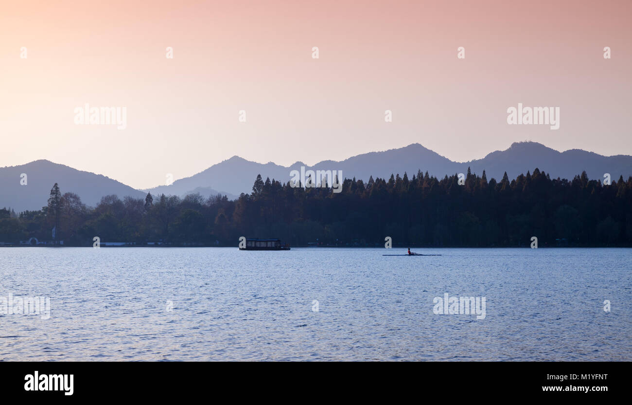 Coastal landscape with rower on West Lake in evening. Popular public park of Hangzhou city, China Stock Photo