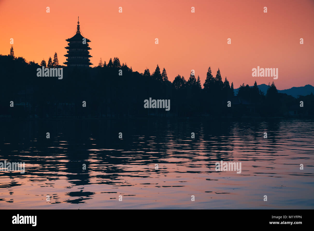 Chinese landscape at sunset, silhouette of ancient pagoda over bright evening sky background. Coast of West Lake. Famous public park in Hangzhou city, Stock Photo