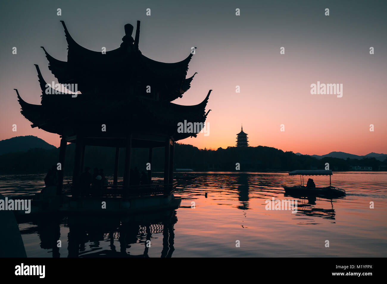 Chinese landscape at sunset, ancient gazebo pavilion and rowing boat on West Lake. Popular public park of Hangzhou city, China Stock Photo