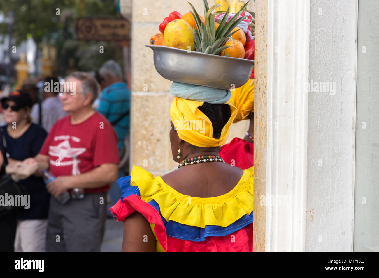 Cartagena, Colombia - January 23th, 2018: rear view of a fruit vendor palenquera with a metal basket with fruits on her head waiting for clients at th Stock Photo