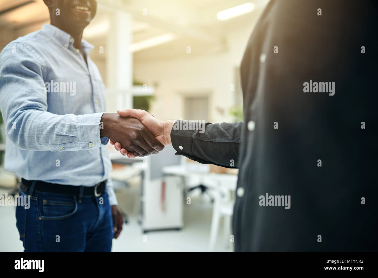 Closeup of two male business colleagues shaking hands together while standing in a modern office Stock Photo