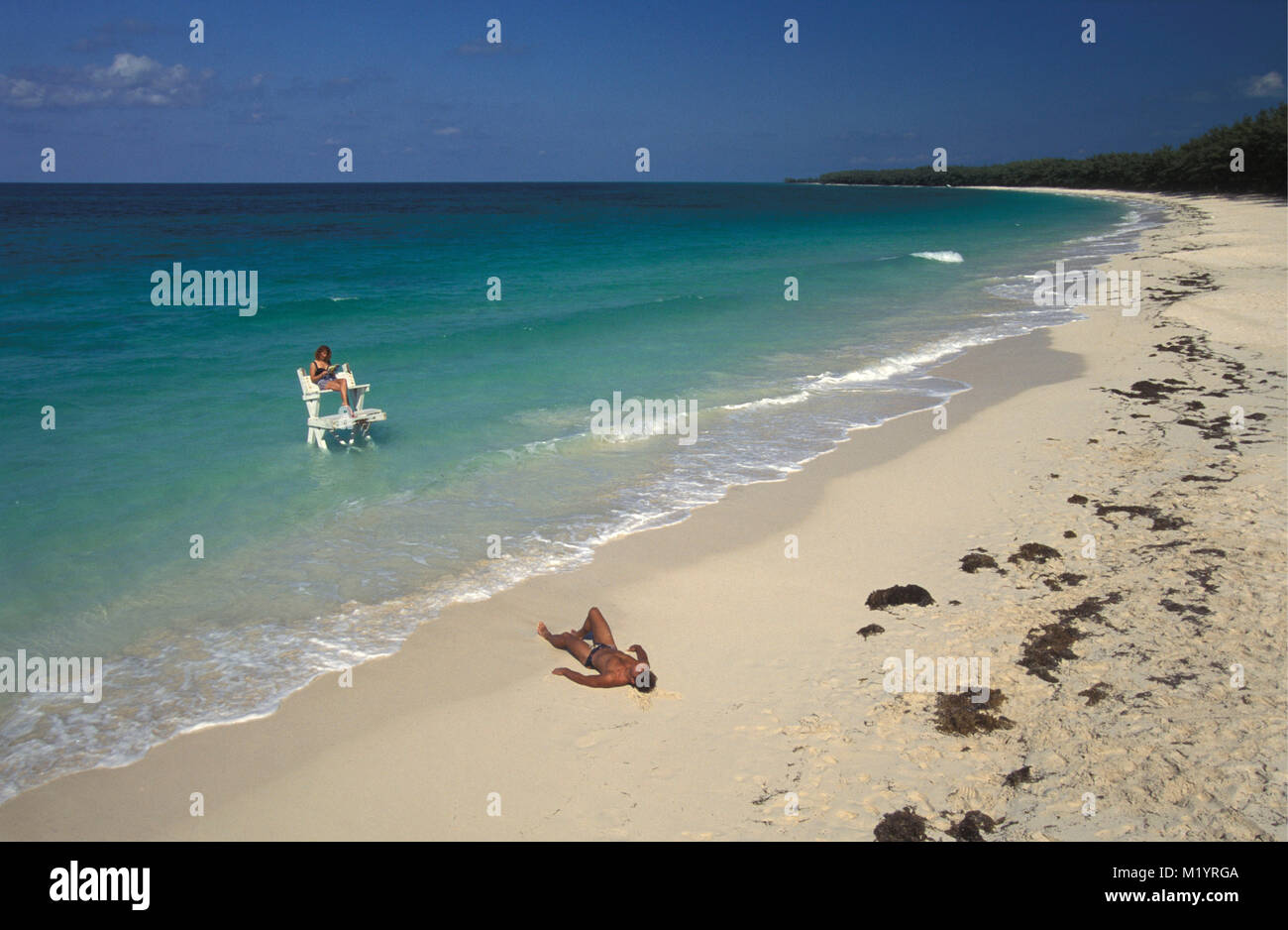 The Bahamas. Bimini Islands. Caribbean island. Woman on beach relaxing on platform in shallow tropical water. Man sunbathing on beach. Stock Photo