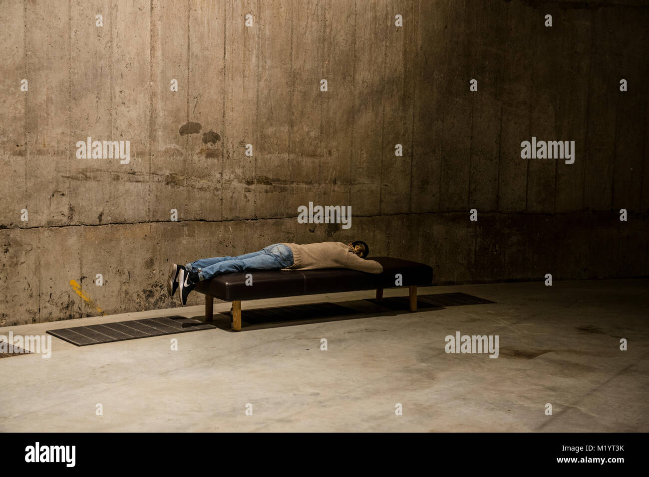 Man lying on bench by concrete wall, Tate Modern, London, England Stock Photo