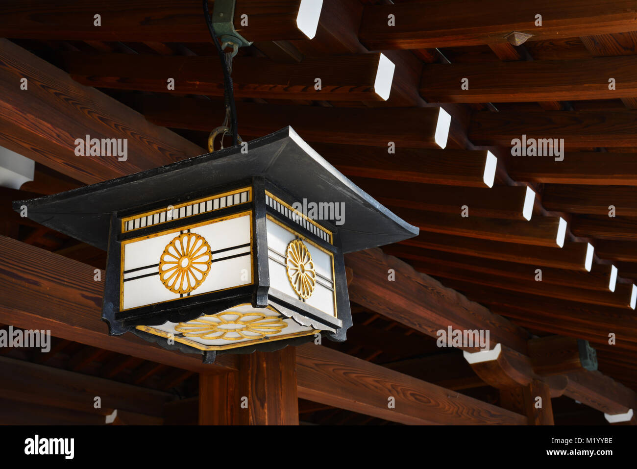 Old japanese lantern with chrysanthemum motif under a traditional wooden roof Stock Photo