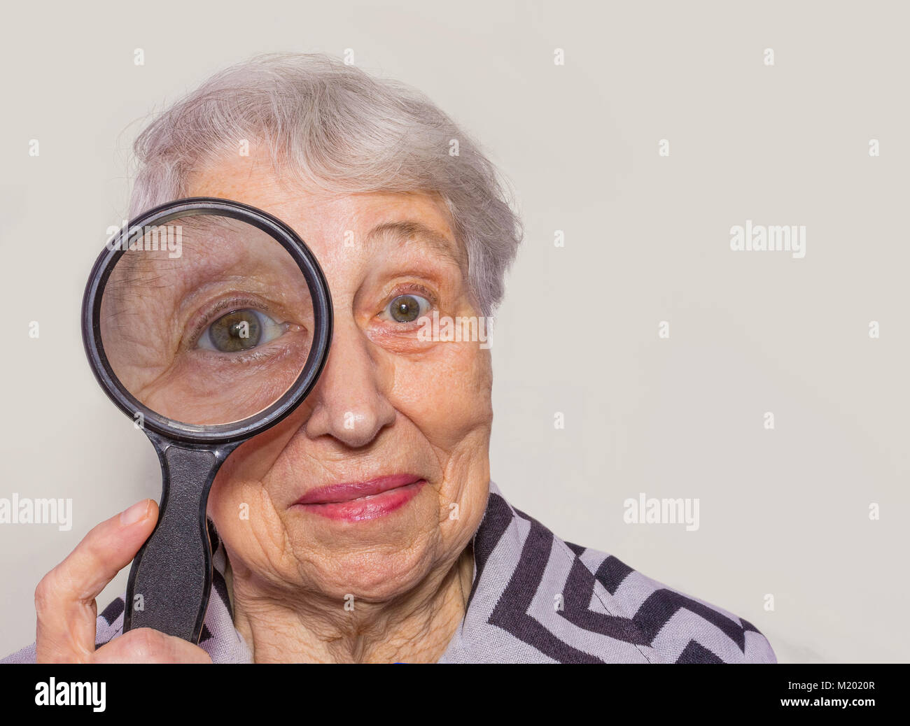 portrait of senior woman looking through a magnifying glass over white background Stock Photo