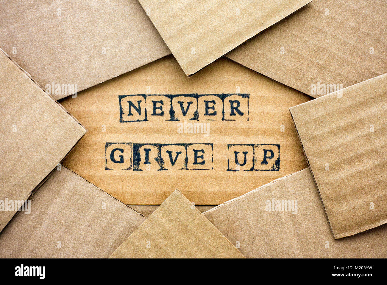 Words Never Give Up make by black alphabet stamps on cardboard with some piece of cardboard. Stock Photo