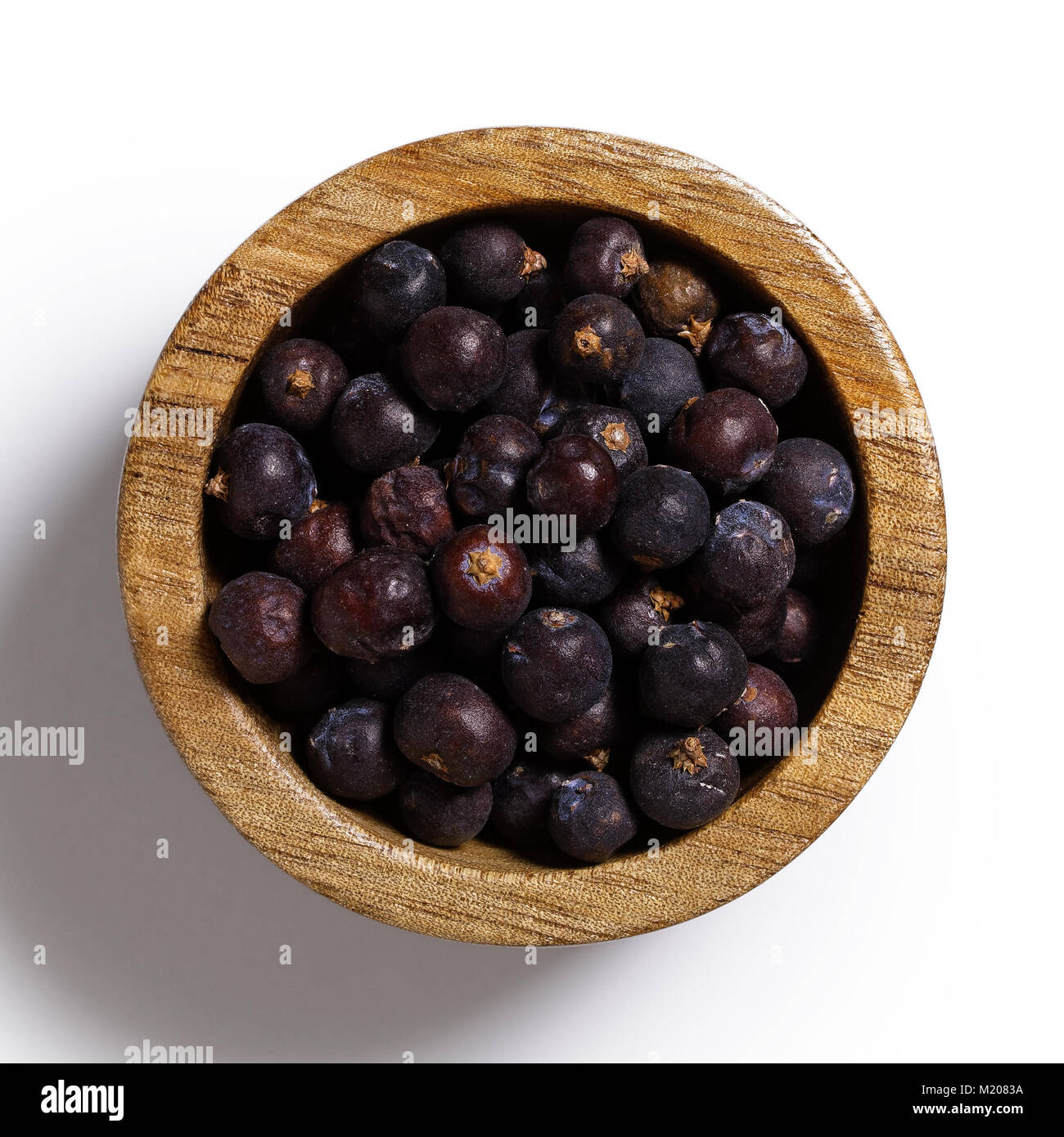 Dry juniper berries in dark wood bowl isolated on white from above. Stock Photo