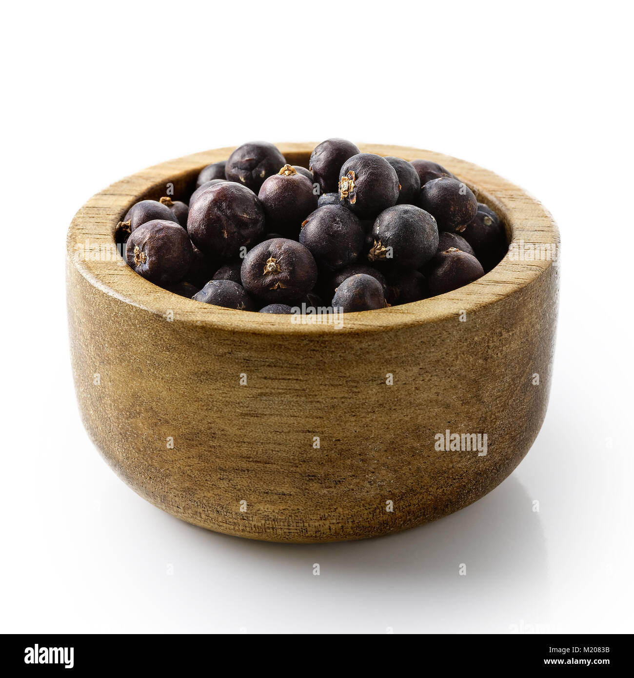 Dry juniper berries in dark wood bowl isolated on white. Stock Photo