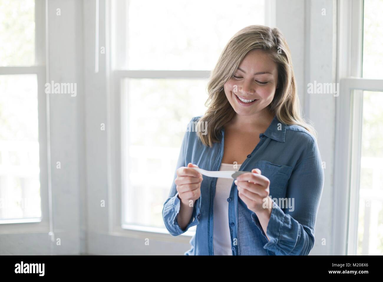 Portrait of young woman with pregnancy test, smiling. Stock Photo