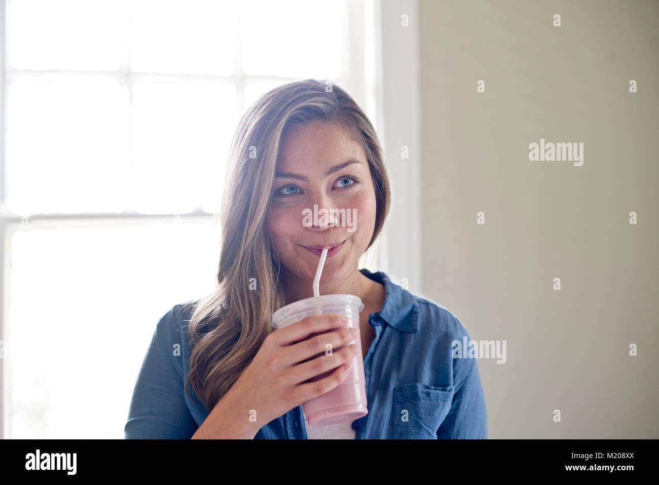 Portrait of young woman drinking through straw. Stock Photo
