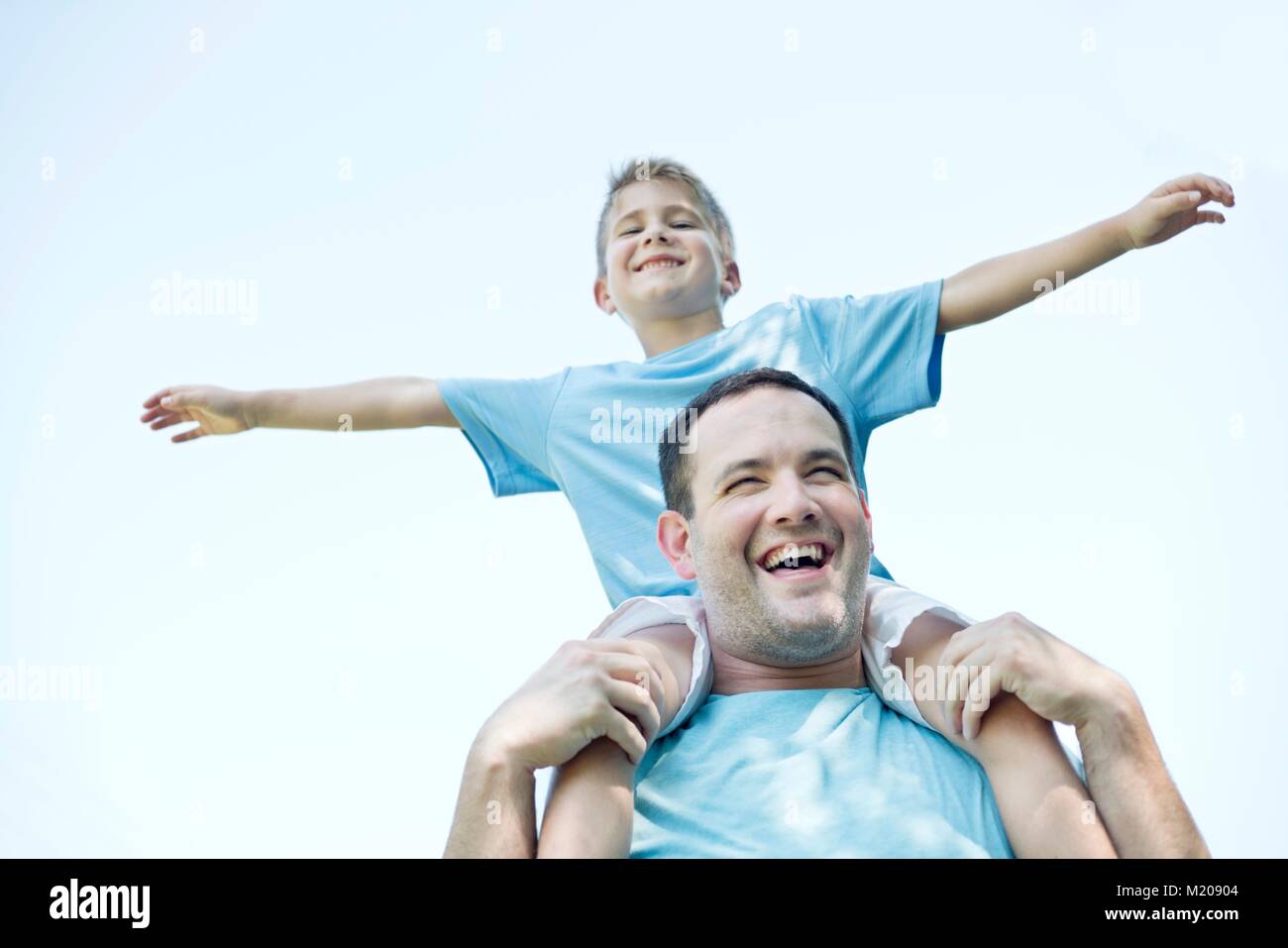 Father carrying son on shoulders, boy with his arms out. Stock Photo