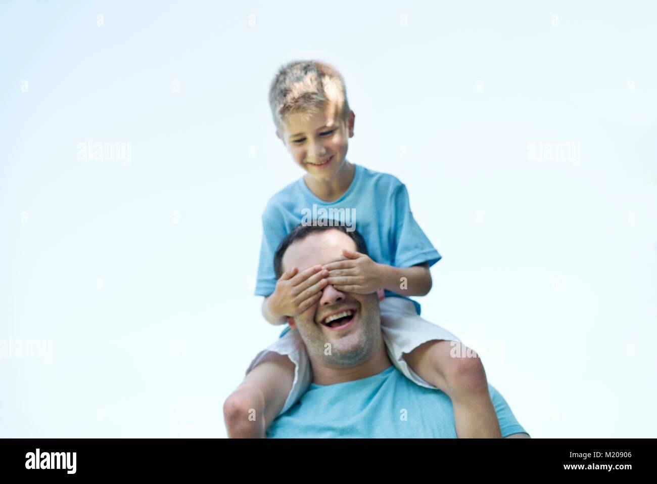 Father carrying son on shoulders, boy covering his father's eyes with hands. Stock Photo