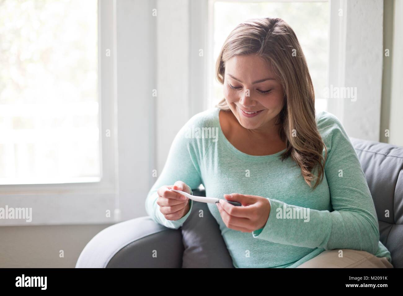 Young woman sitting on sofa and looking at pregnancy test. Stock Photo