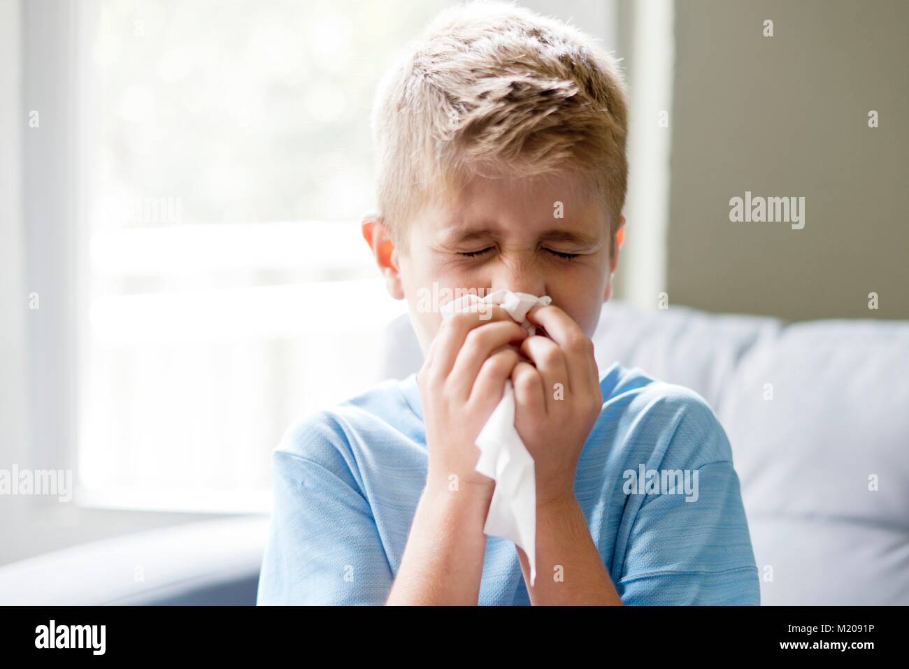 Young boy blowing his nose on a tissue. Stock Photo