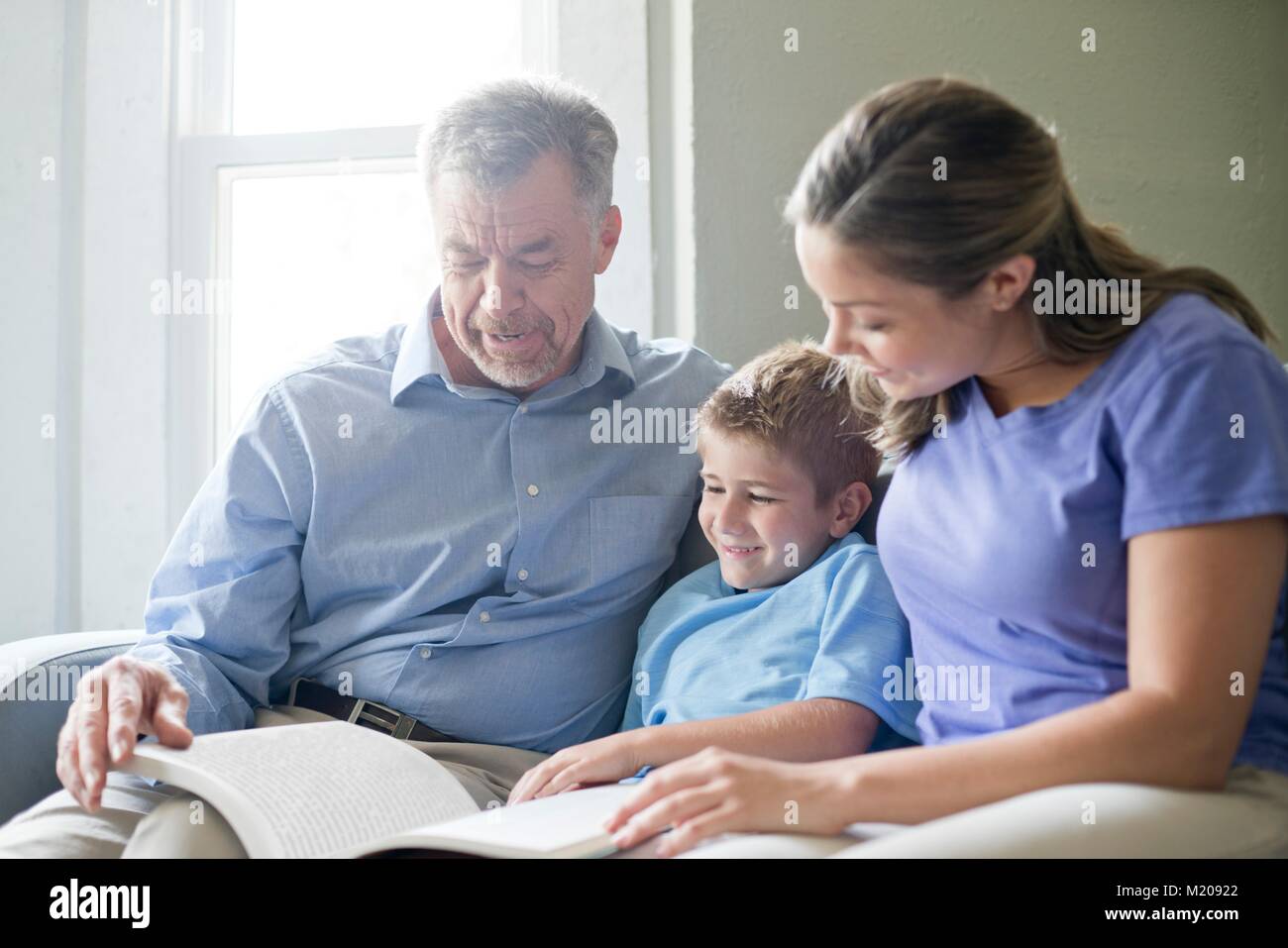 Boy reading a book with his grandfather and his mother. Stock Photo