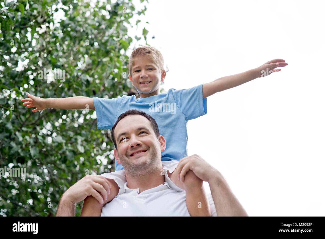 Father carrying son on shoulders with arms out. Stock Photo