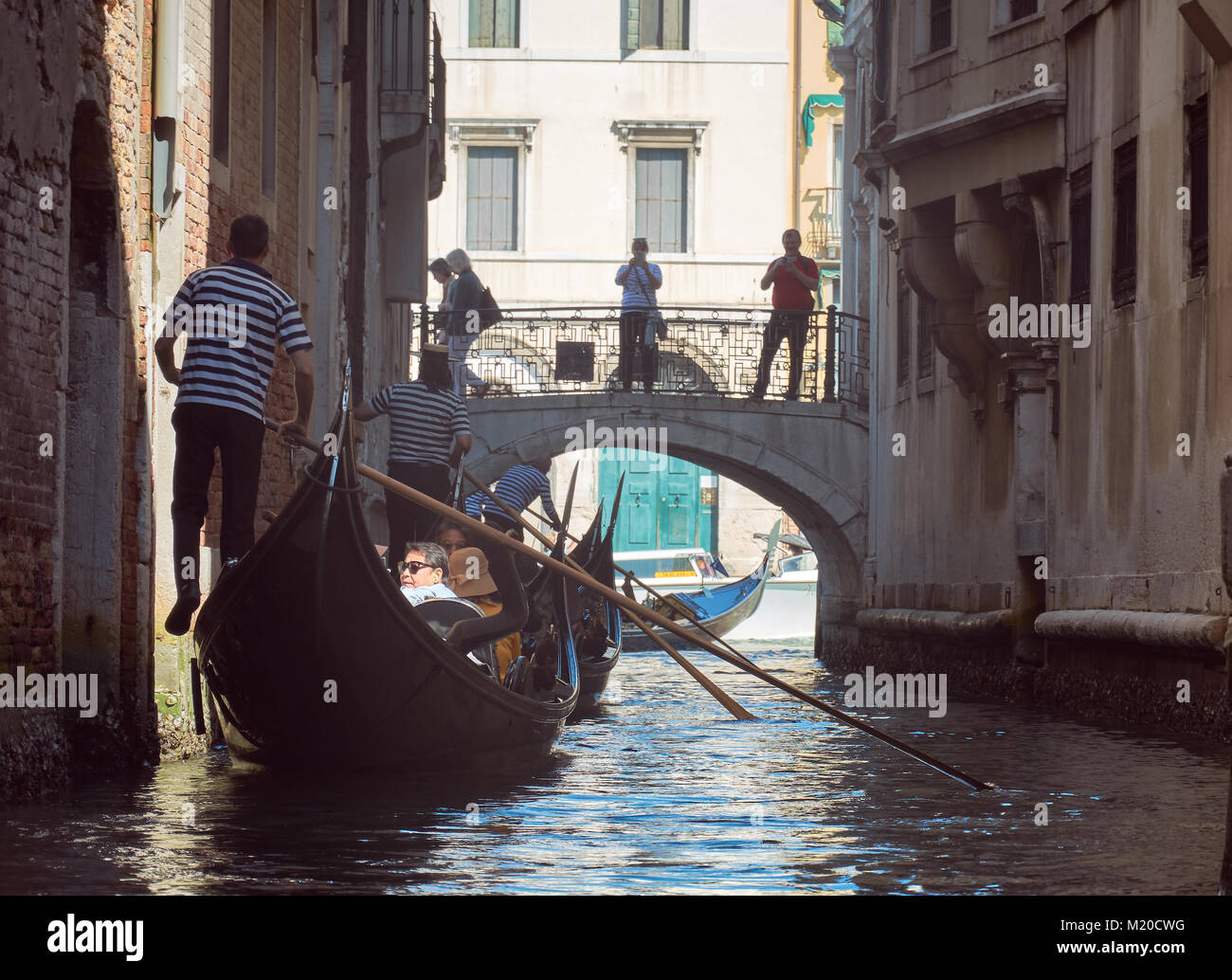 VENICE, ITALY - MAY 21, 2017: Gondolas, tourists, old buildings and a bridge seen from a gondola, reaching the Grand Canal, in Venice, Italy. Stock Photo