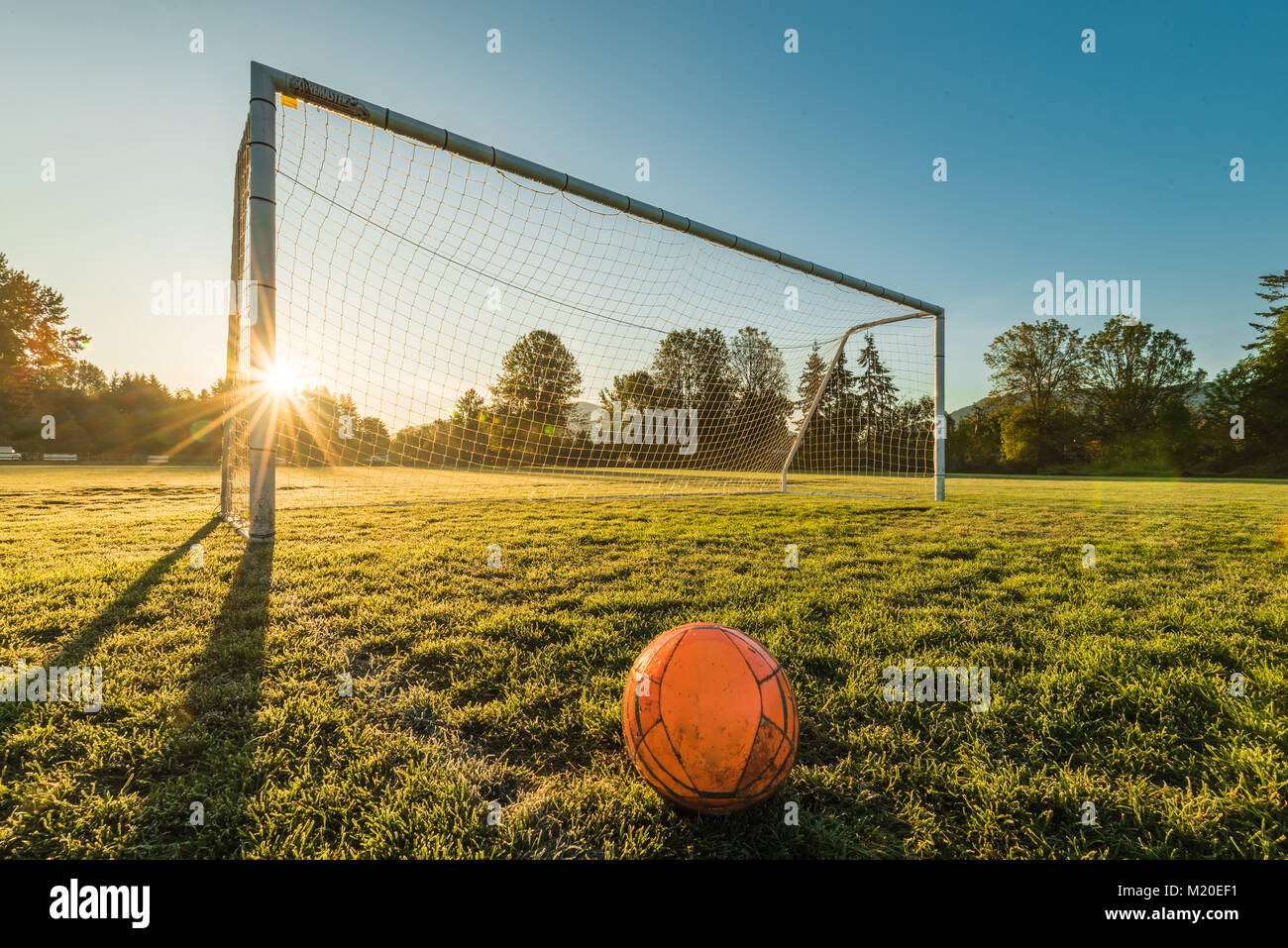 Vibrant soccer ball off centered in front of soccer goal at sunrise Stock Photo