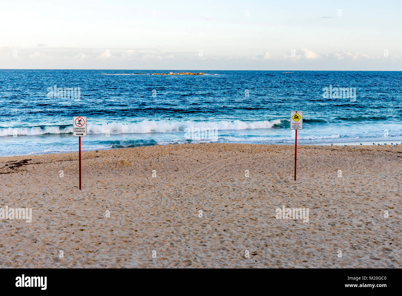 Empty beach, calm blue Pacific Ocean, signposts, sunny day. Footsteps on beach, tranquil Tasman sea, danger sign, Coogee Beach, Sydney, Australia. Stock Photo