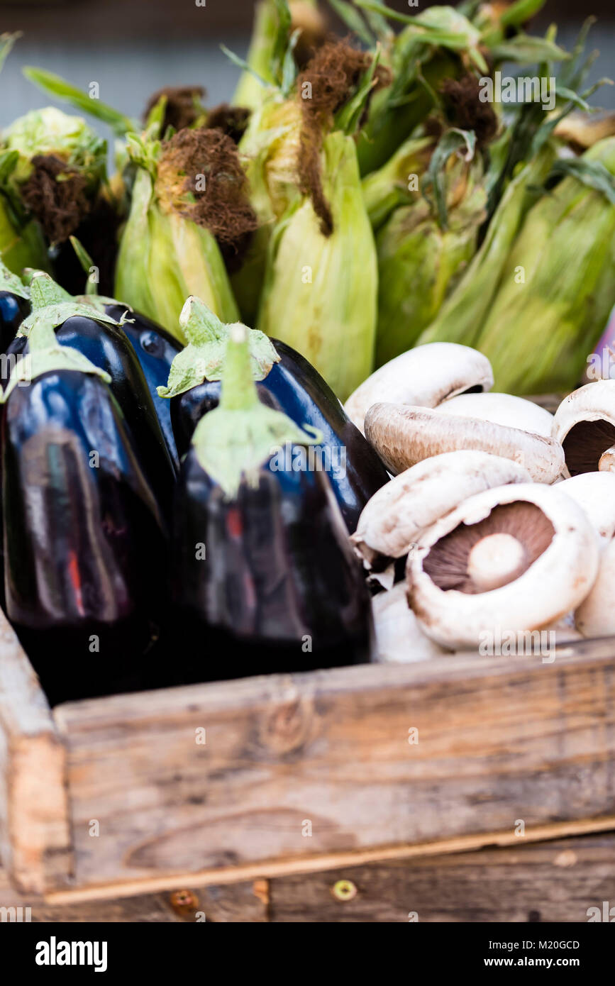 Organic fresh vegetables in wooden basket displayed at market, closeup. Eggplant, mushroom, corn cobs at market stall, Sydney, Australia. Stock Photo