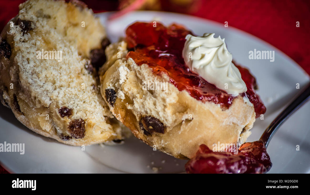 Scone with whipped cream and strawberry jam, food macro, selective focus. Afternoon tea, pastry on white plate red background, low key. Stock Photo